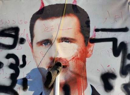 A slipper hangs on a vandalised poster of Syrian President Bashar al-Assad lying in a trash container in Aleppo, Syria