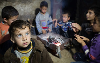 Syrian children warm their hands around a coal fire