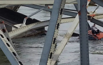A man sits on the roof of his car awaiting rescure after the bridge collapse