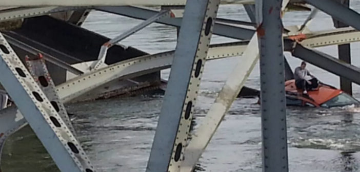 A man sits on the roof of his car awaiting rescure after the bridge collapse
