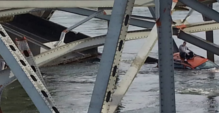 A man sits on the roof of his car awaiting rescure after the bridge collapse